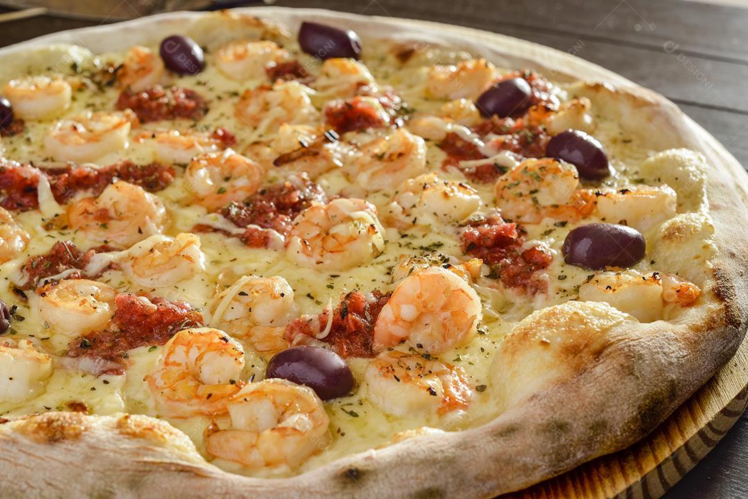 Pizza de camarão com azeitonas em close-up de pá de madeira.