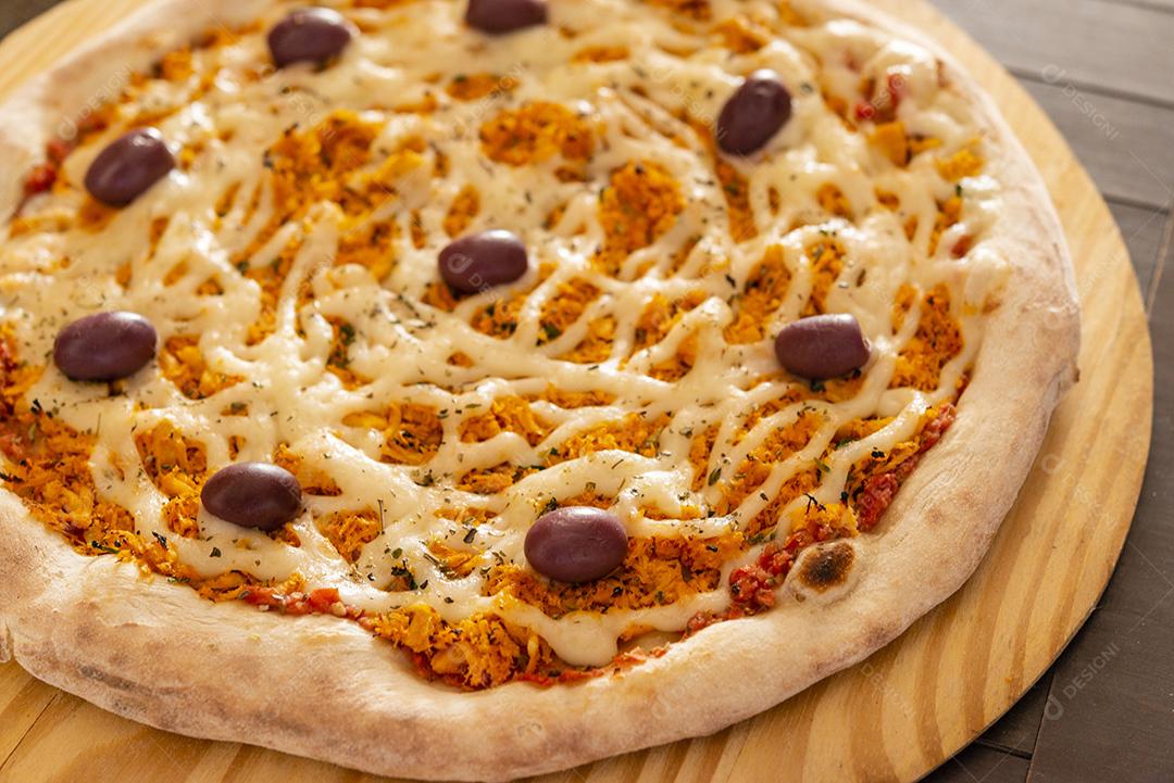 Pizza de frango com catupiry e azeitonas em close-up de pá de madeira.