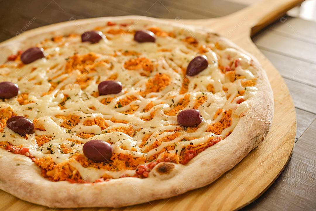 Pizza de frango com catupiry e azeitonas em close-up de pá de madeira.