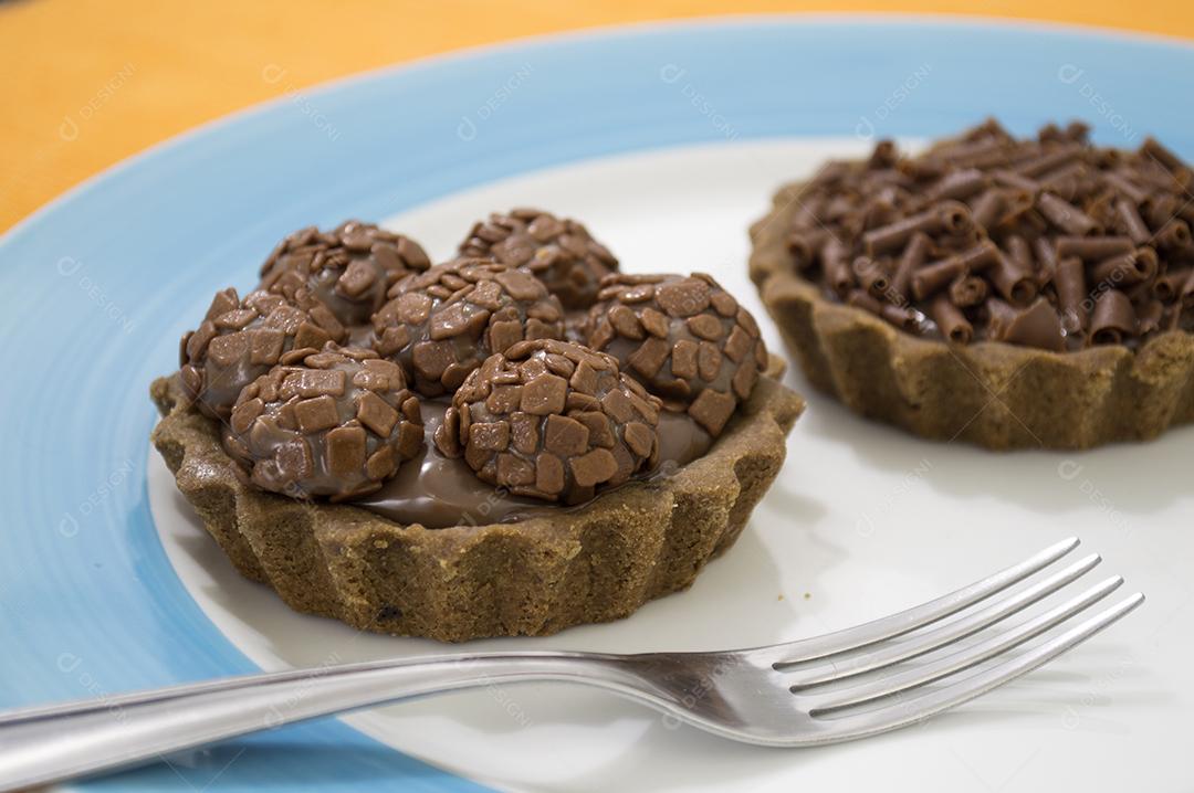 Tartelettes de chocolate e fudge sobre prato branco e azul.