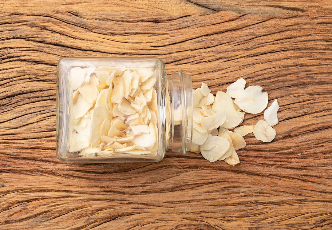 Closeup de fatias de alho secas em uma panela de vidro sobre a mesa de madeira.