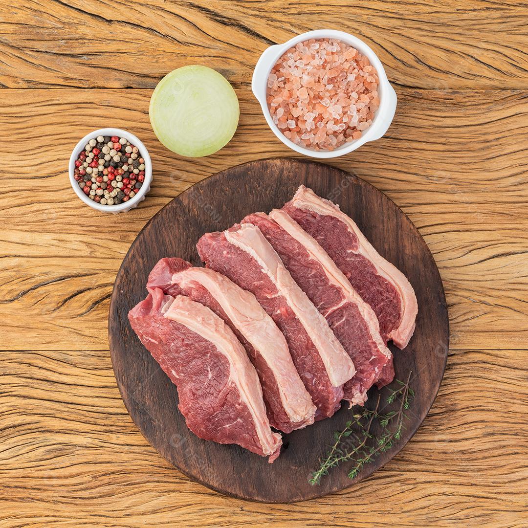 Fatias de lombo de tira crua sobre tábua de madeira com temperos.