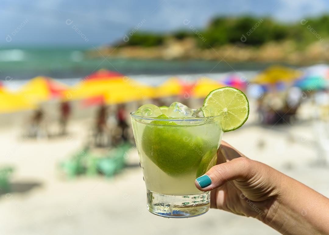 Beba caipirinha. Mão segurando uma bebida caipirinha em uma praia