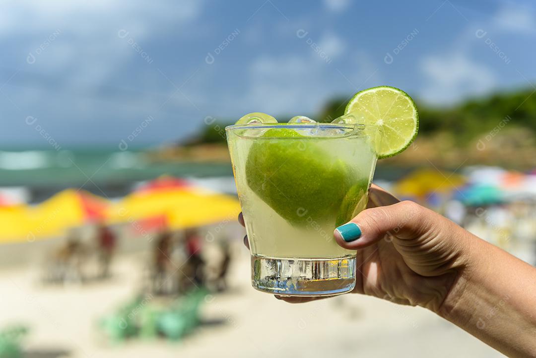Beba caipirinha. Mão segurando uma bebida caipirinha em uma praia
