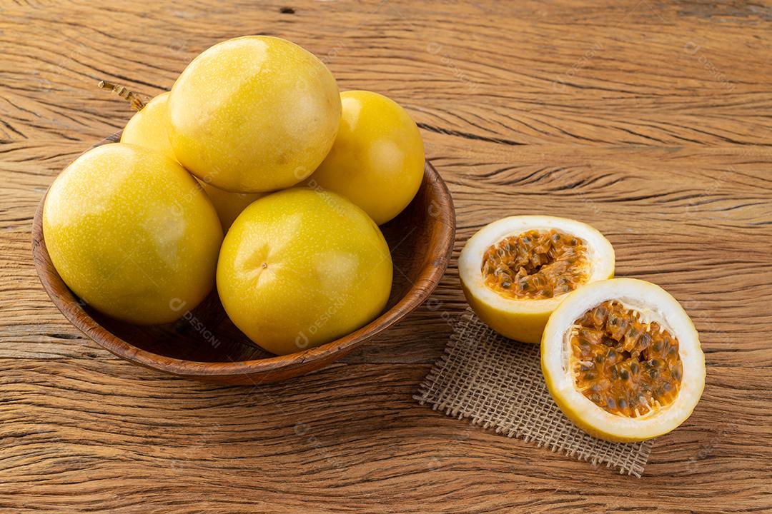 Maracujás em uma tigela com frutas cortadas sobre a mesa de madeira.