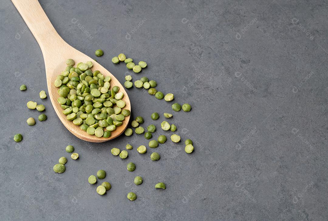 Ervilhas verdes secas cruas em uma colher sobre fundo de pedra.