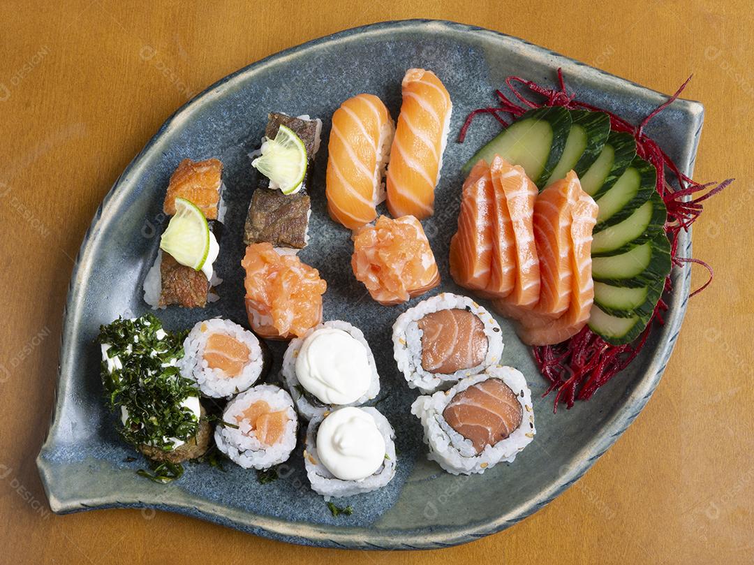 Sushi, sashimi, pãezinhos e legumes prato em forma de folha sobre a mesa de madeira