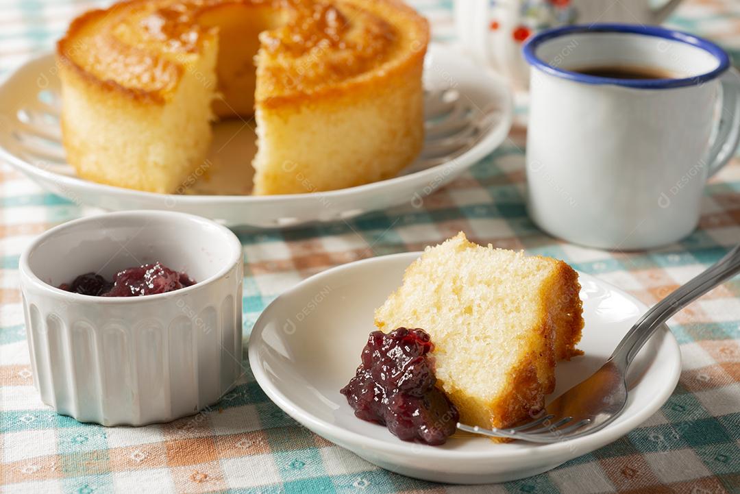 Bolo, bolo fatiado, geléia de frutas e uma xícara de café sobre têxteis xadrez