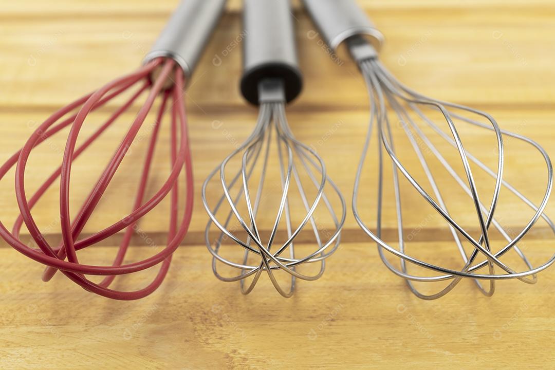 Três fouets de cozinha sobre a mesa de madeira.