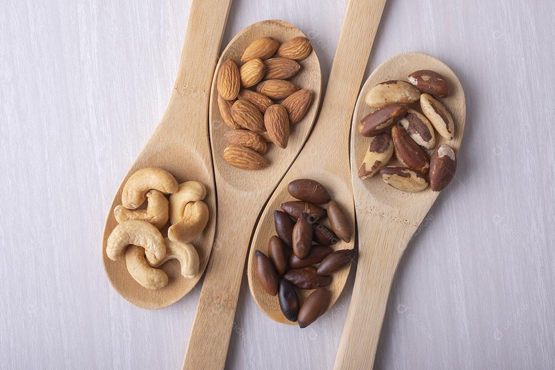 Quatro colheres de pau com castanhas, cajus, barus e amêndoas.