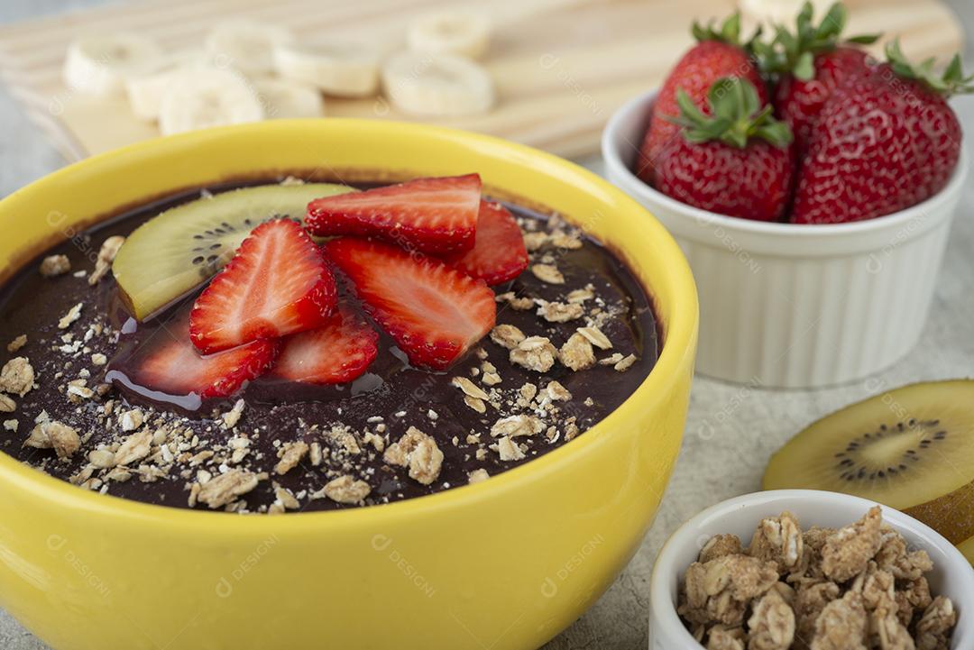 Tigela de açaí típica brasileira com frutas e muesli sobre fundo de madeira.