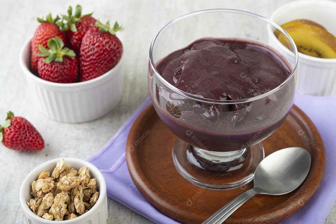Tigela de açaí típica brasileira com frutas e muesli sobre fundo de madeira.