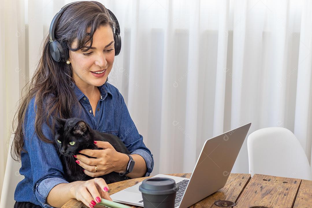 Mulher mexendo no notebook segurando um gato preto