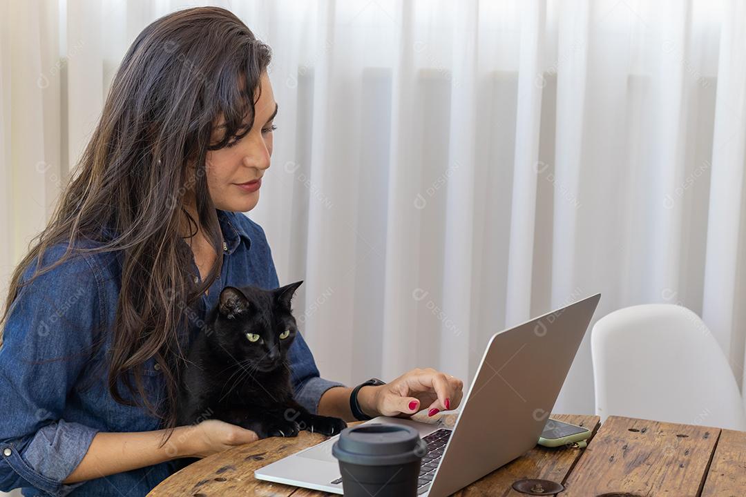 Mulher mexendo no notebook segurando um gato preto