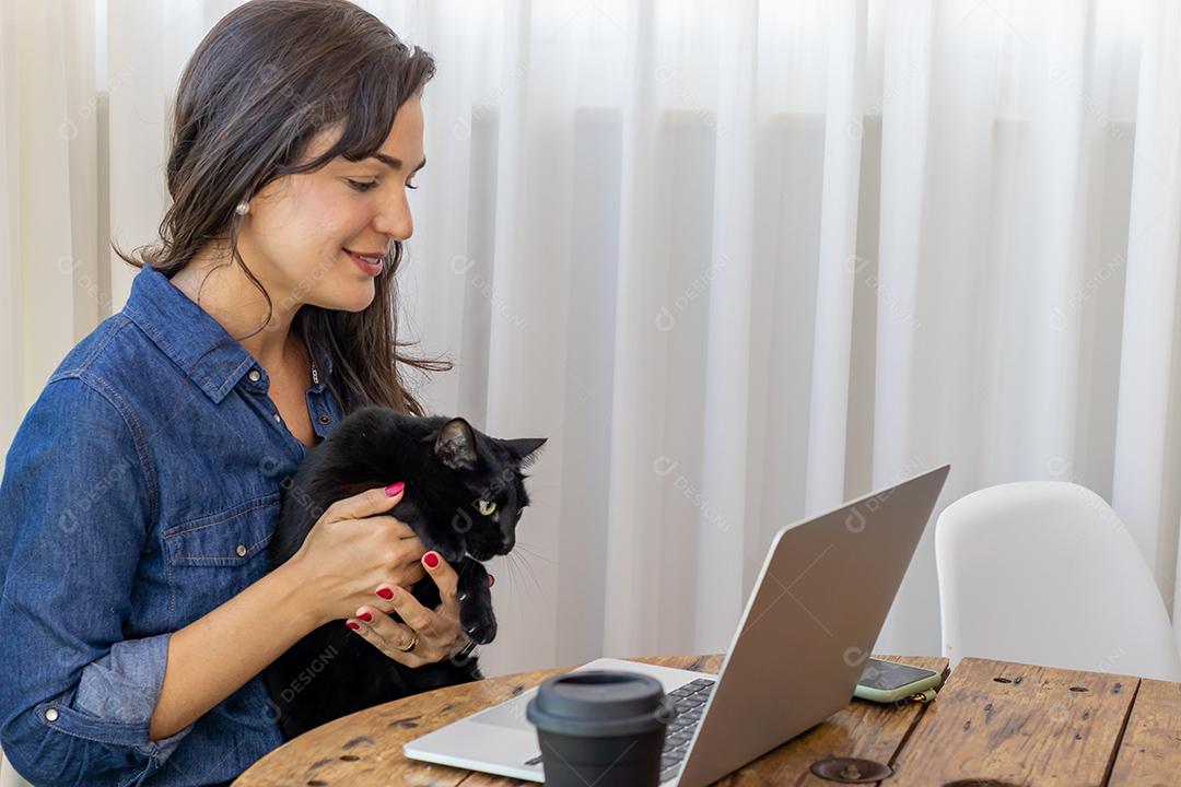 Mulher mexendo no notebook segurando um gato preto