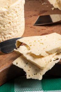 Queijo semi-curado do Brasil disposto em uma tábua rústica sobre uma toalha de mesa