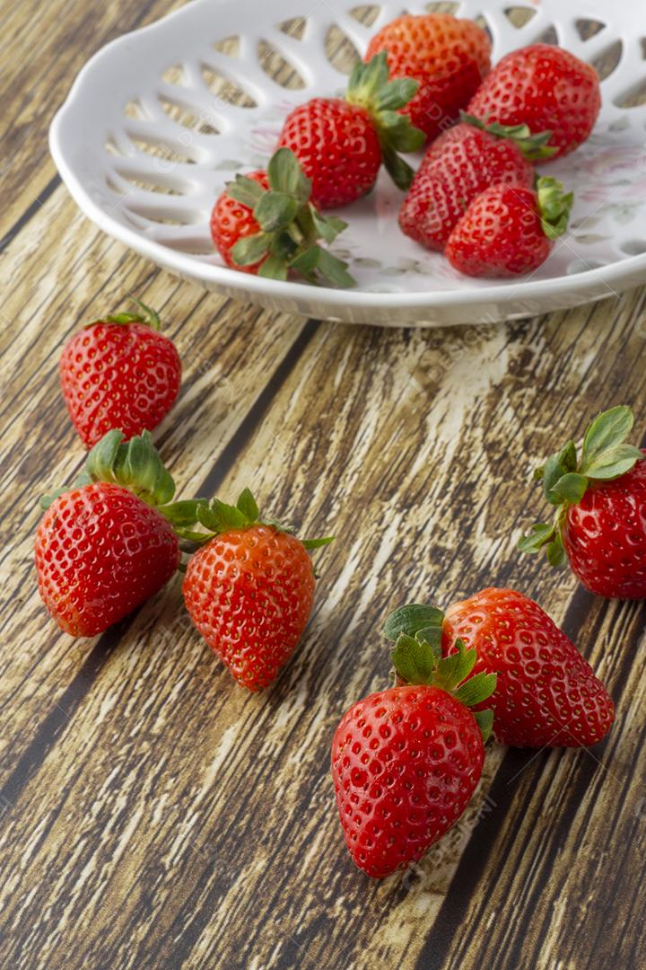 Morangos em um prato decorado e sobre uma mesa de madeira