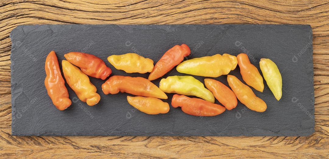 Pimentas de laranja em uma tábua de pedra sobre mesa de madeira