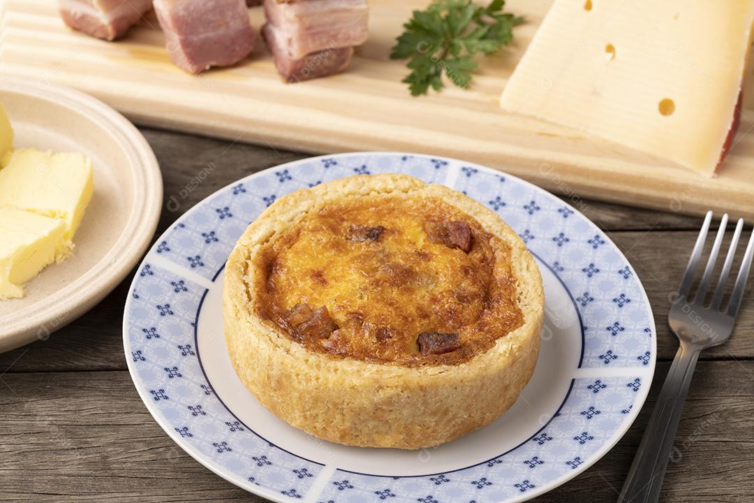 Quiche lorrane caseiro sobre tábua de madeira com ingredientes