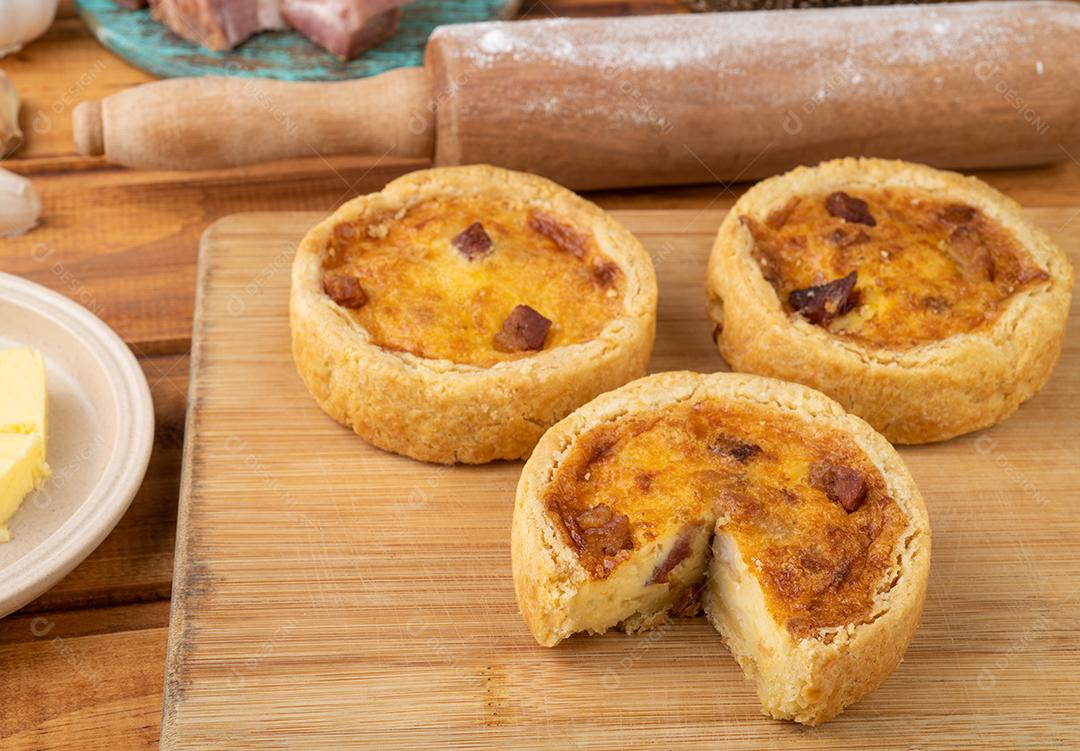 Quiche lorrane caseiro sobre tábua de madeira com ingredientes