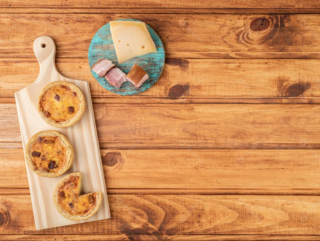 Quiche lorrane caseiro sobre tábua de madeira com ingredientes