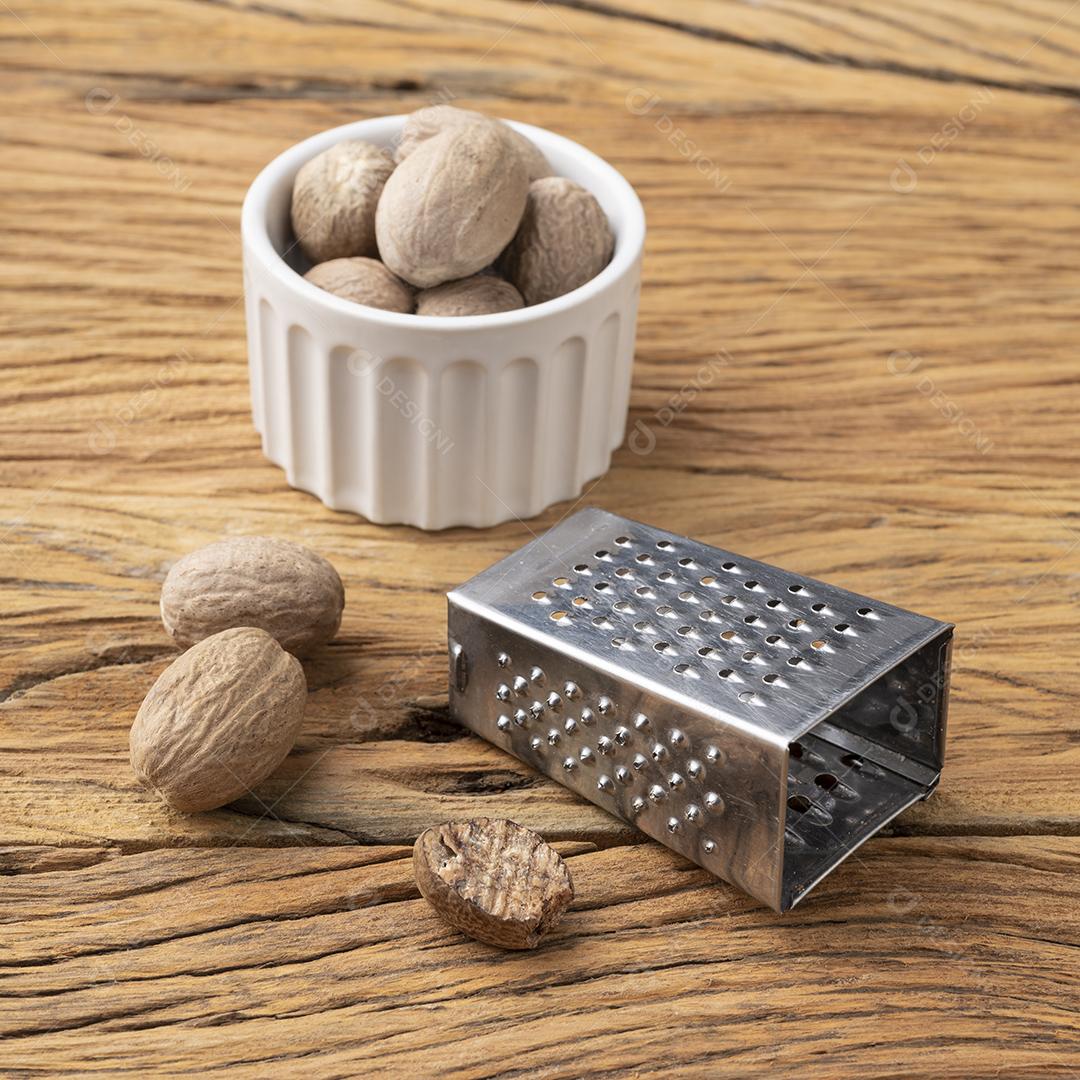 Noz-moscada com ralador sobre mesa. Nozes em uma tigela