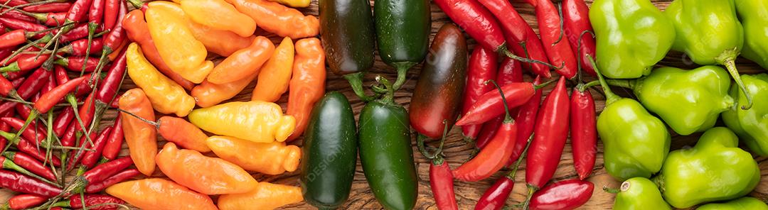 Pimentões variados sobre mesa de madeira, formato panorâmico