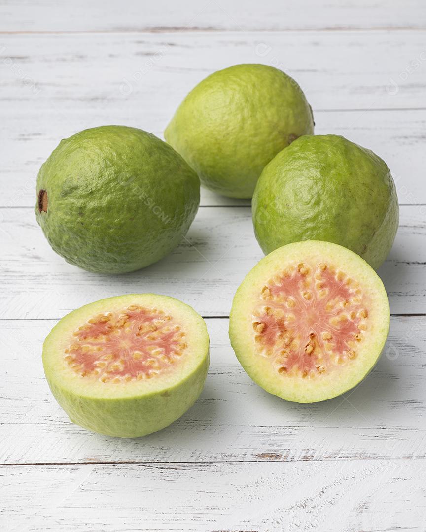 Goiabas vermelhas e meias frutas sobre mesa de madeira