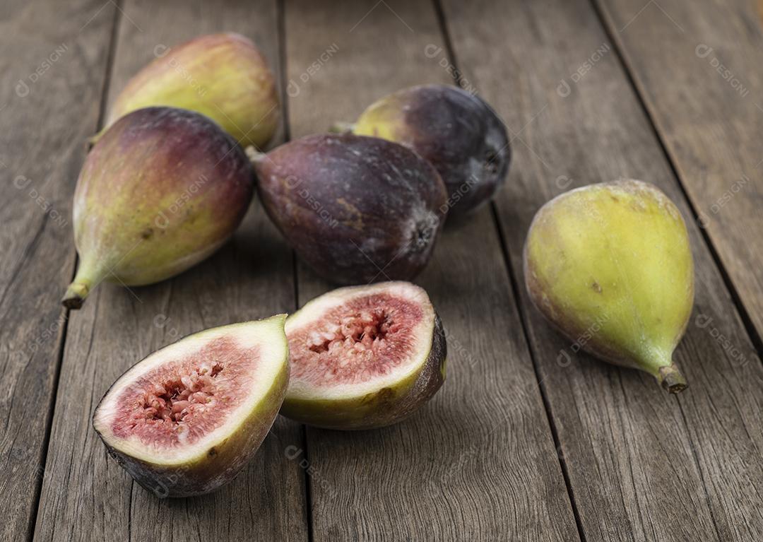 Um grupo de figos sobre mesa de madeira com frutas cortadas