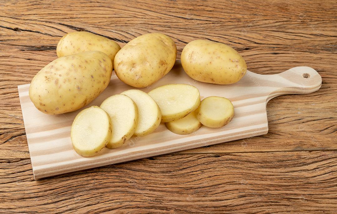 Batatas cruas com fatias em uma tábua de corte sobre mesa de madeira