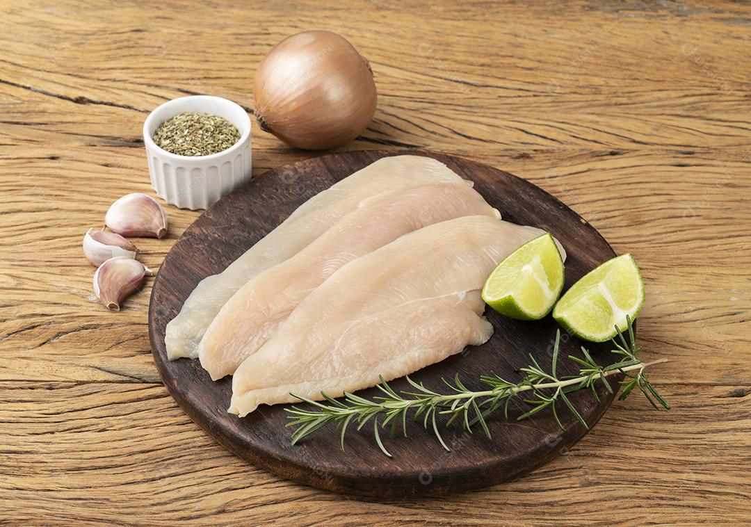 Peito de frango sobre tábua de madeira com temperos