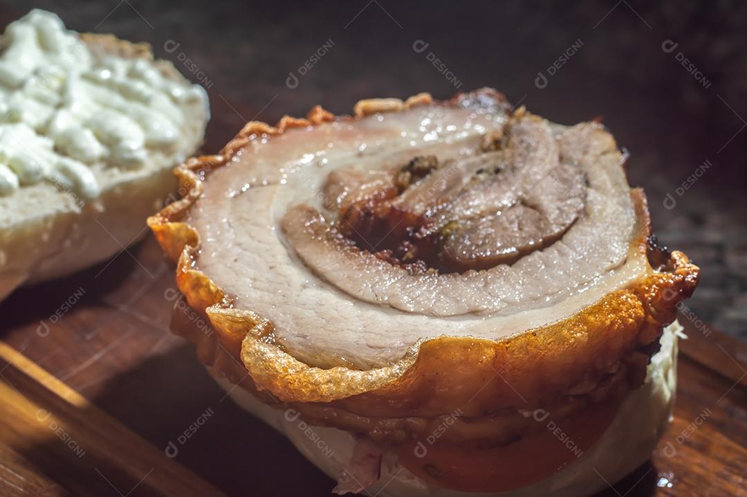 Porchetta, sanduíche de porchetta sendo montado em uma mesa de madeira, ao lado de folhas de pão e rúcula.