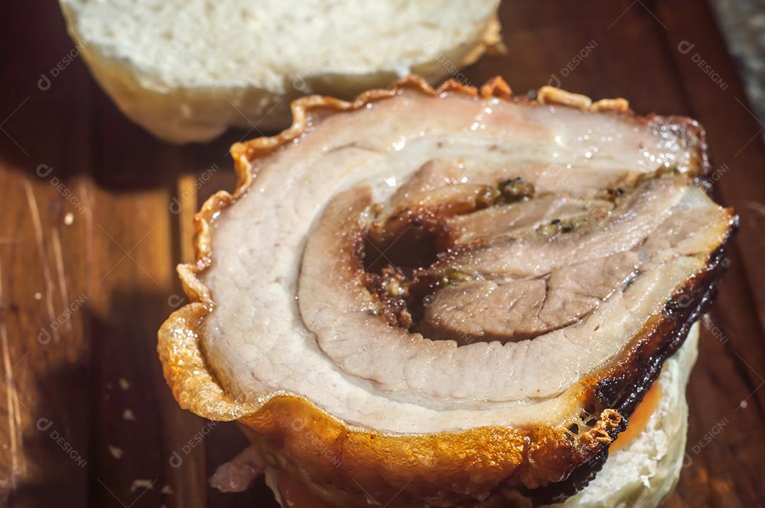 Porchetta, sanduíche de porchetta sendo montado em uma mesa de madeira, ao lado de folhas de pão e rúcula.