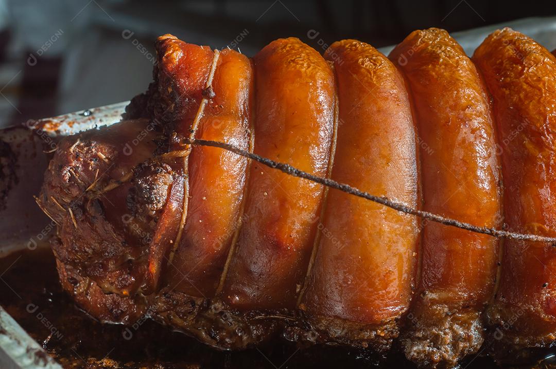 Porchetta inteira assada e defumada, com casca avermelhada, colocada em uma assadeira