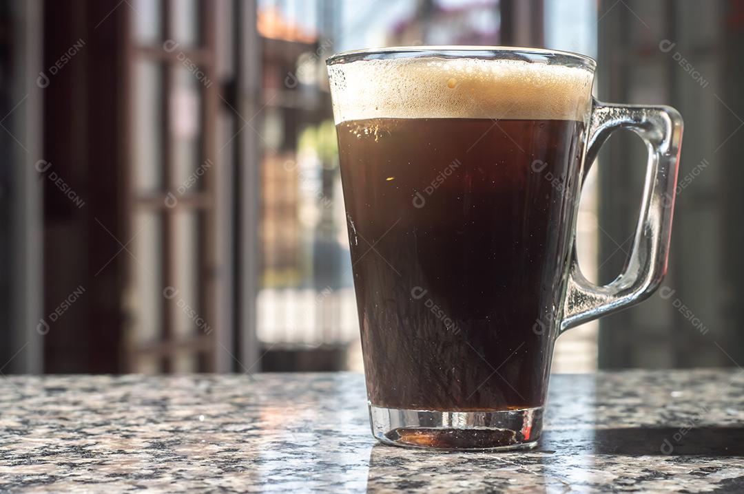 Café tônico em xícara transparente que fica sobre uma mesa de marmore