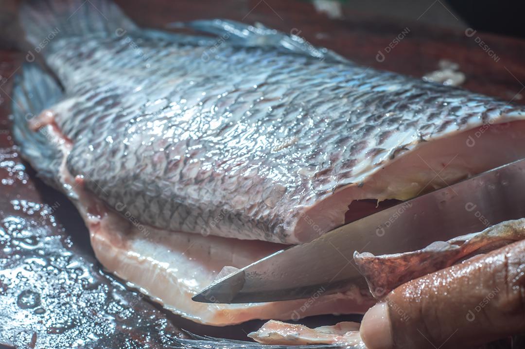 Peixe tilápia usando uma faca, homem limpando um peixe em uma mesa