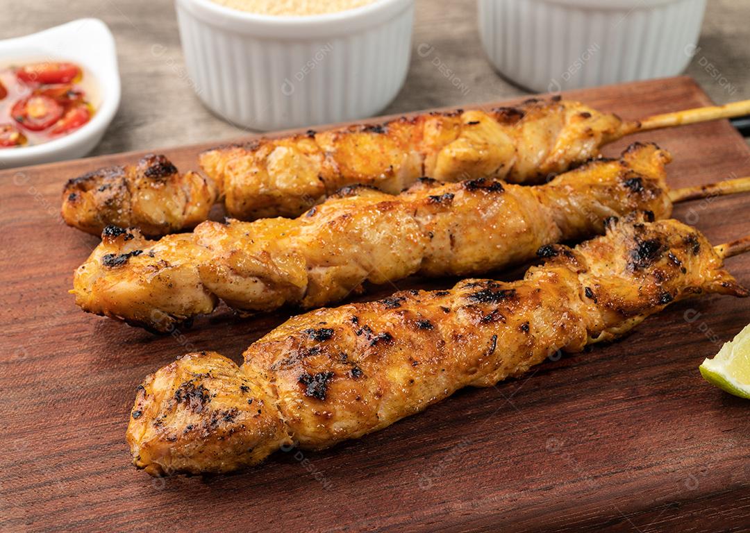 Espetinhos de frango sobre tábua de madeira com farofa, limão e pimenta