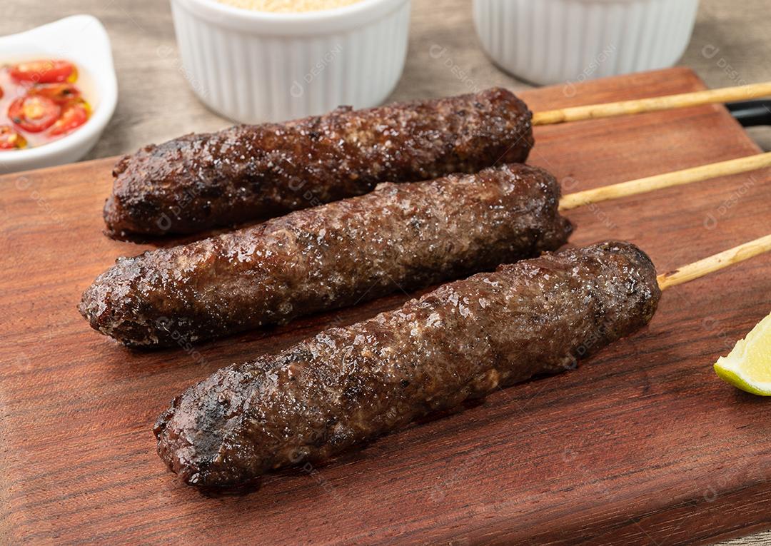 Espetinhos de Kafta de carne sobre tábua de madeira com farofa, limão e pepp