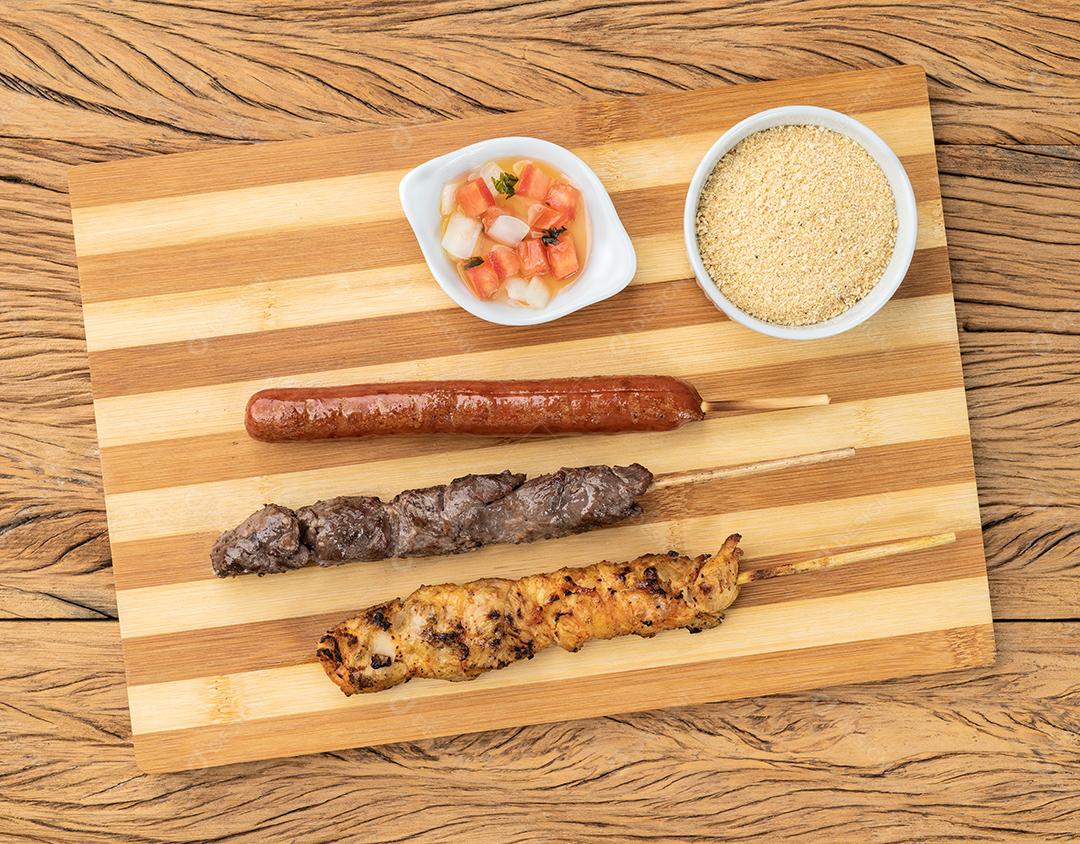 Espetos de salsicha de carne, frango e porco sobre placa de madeira com fa