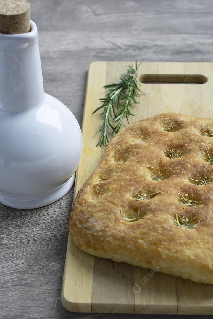 Focaccia de alecrim sobre placa de madeira com garrafa de azeite