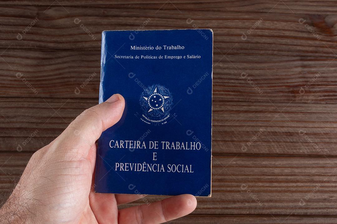 Mão segurando carteira de trabalho brasileira em fundo de madeira