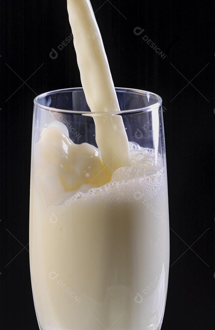Leite sendo derramado em copo de vidro no fundo preto