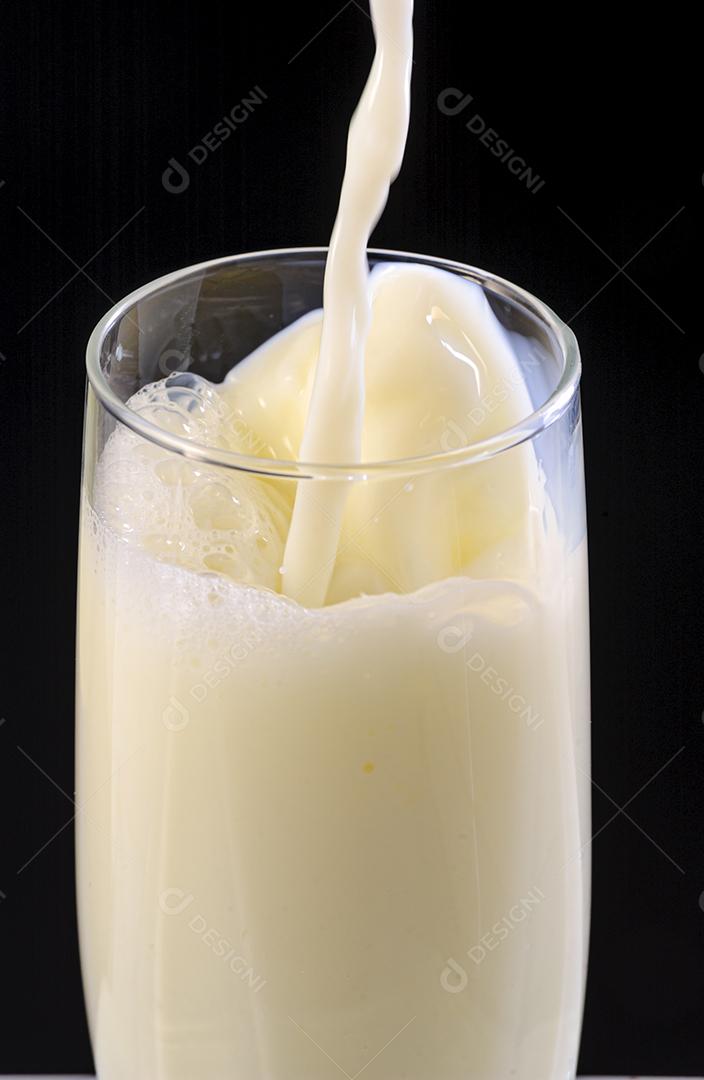 Leite sendo derramado em copo de vidro no fundo preto