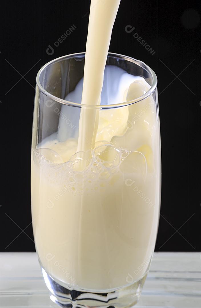 Leite sendo derramado em copo de vidro no fundo preto