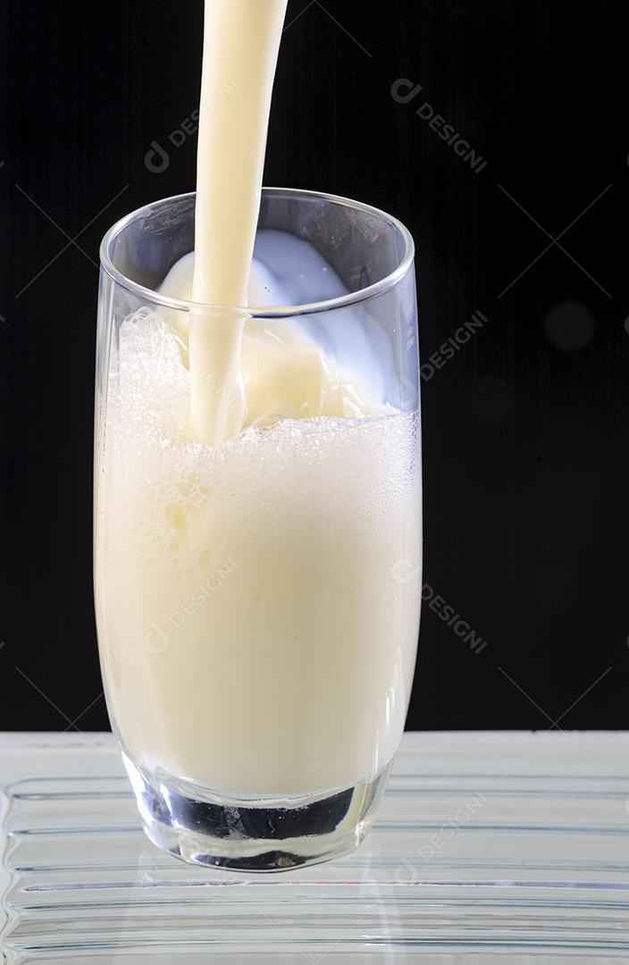 Leite sendo derramado em copo de vidro no fundo preto