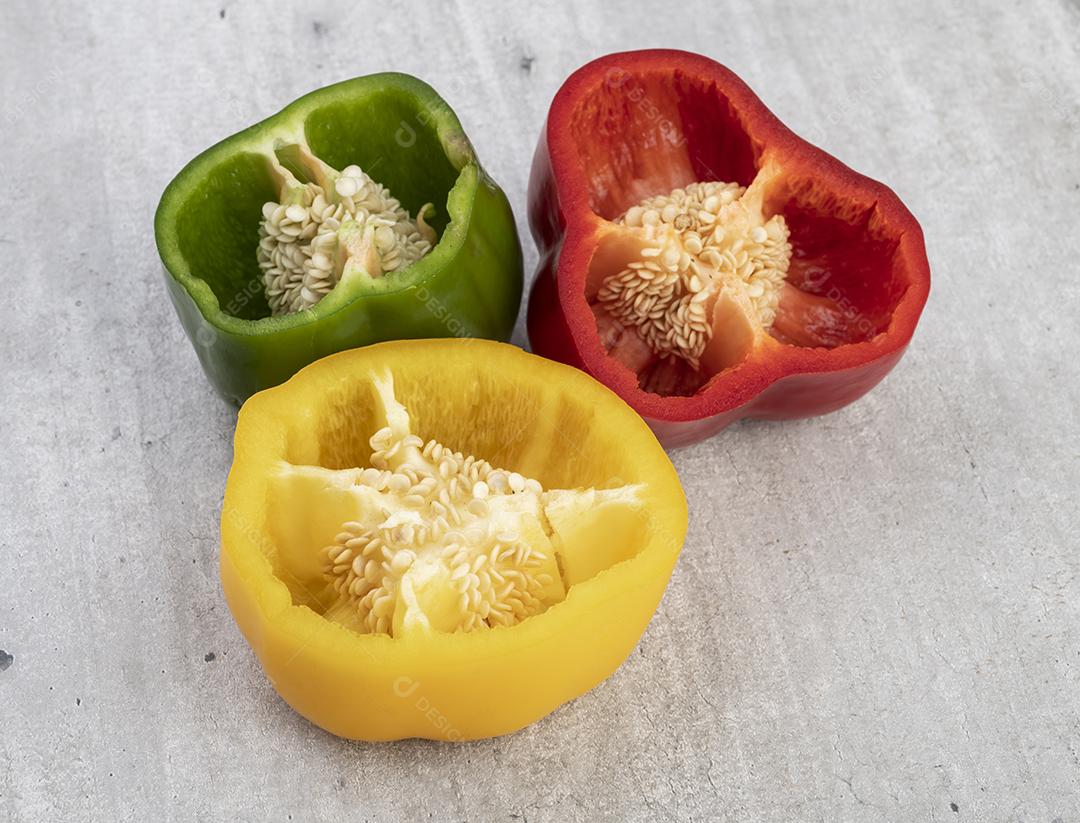 Pimenta de sino verde, vermelha e amarela metades sobre fundo rústico