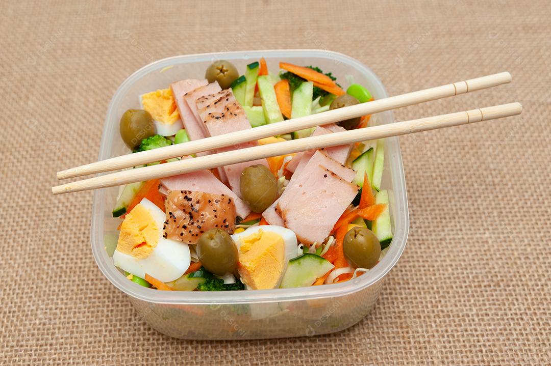 Salada de frango saudável com legumes em recipiente plástico com pauzinho