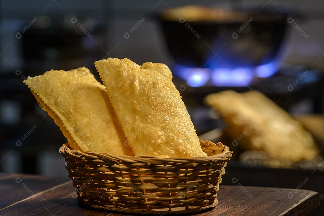 Pastéis brasileiros na cesta com cozinha desfocada ao fundo.