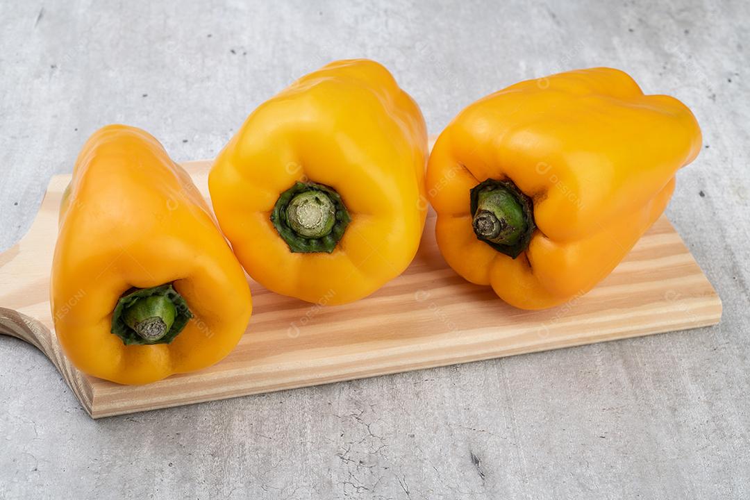 Três pimentões amarelos sobre tábua de madeira