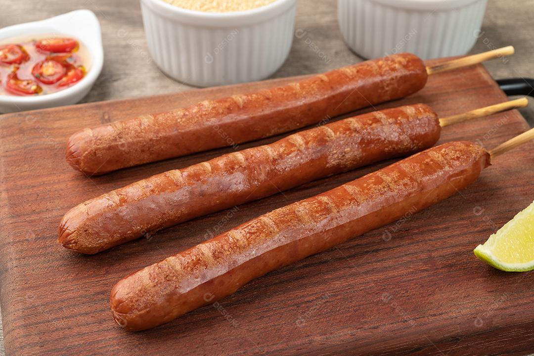 Espetos de salsicha de porco sobre tábua de madeira com limão farofa